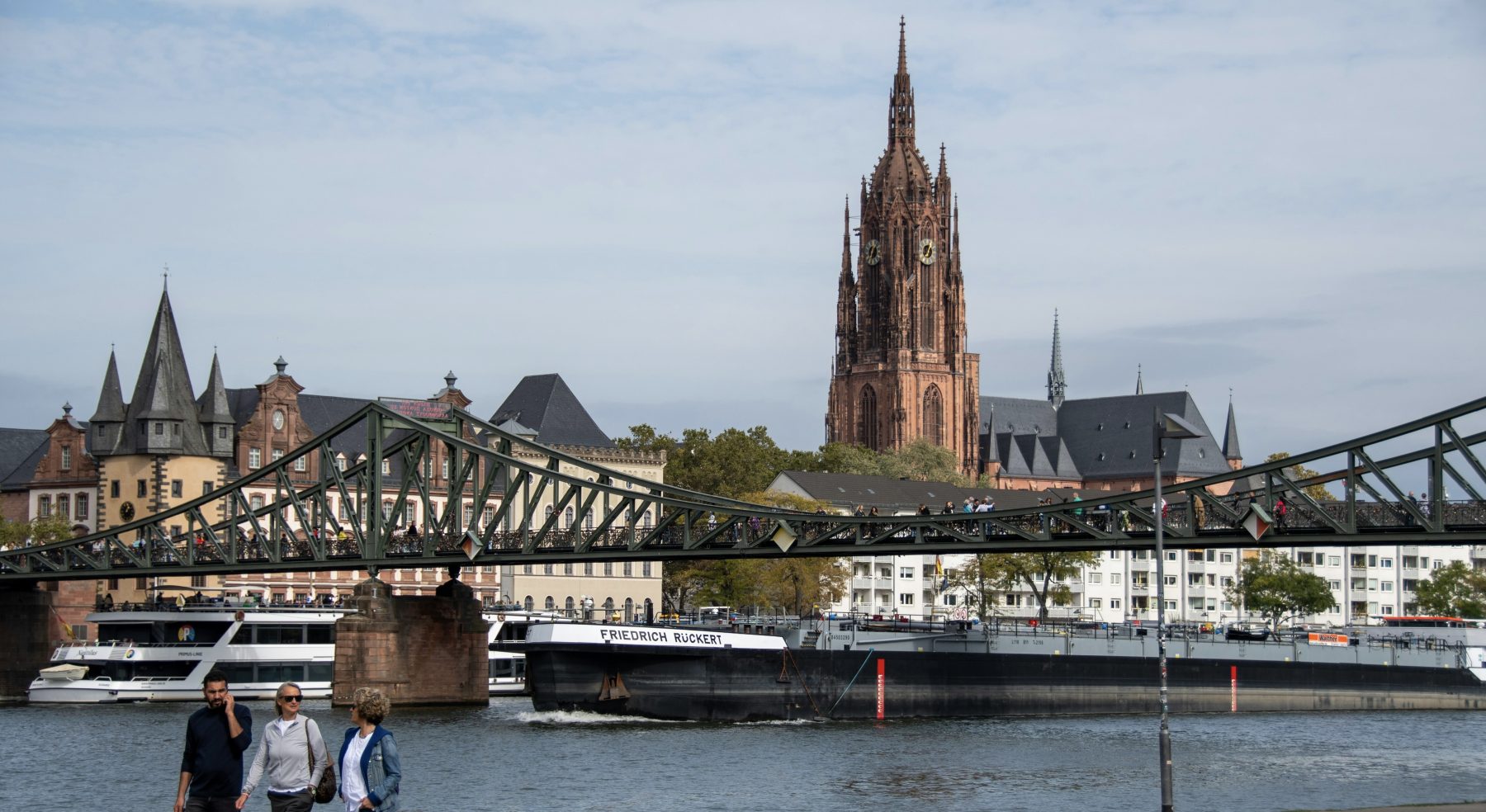 Uitzicht op een brug in Maastricht met op de voorgrond drie wandelaars.