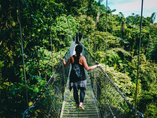 Een vrouw in een zwart shirt en een zwarte broek die op een hangbrug in Costa Rica staat, waar Pura Vida een populaire levenshouding is.